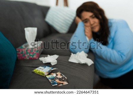 Focus on foreground of a sad depressed woman crying using tissues with a broken picture of her partner after a breakup