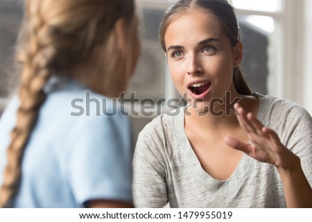Focus on friendly teacher educating autistic little girl who is deaf and using sign language gestures young mother playing with daughter emotionally gesticulating concept image.