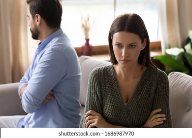 Focus on frustrated frowning young woman sitting separately from upset husband boyfriend on sofa after clarifying relationships at home. Stressed depressed couple ignoring each other after quarrel. - Shutterstock ID 1686987970