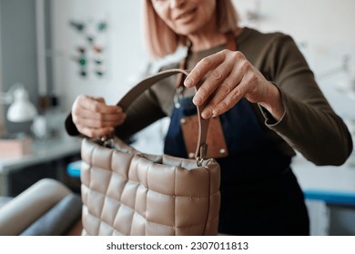 Focus on hand of creative craftswoman holding new handmade leatherwear item while working over order of client in workshop - Powered by Shutterstock