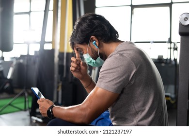 Focus On Hand, Young Indian Body Builder With Medical Face Mask Cleaning Sweat While Using Mobile Phone At Gym - Concept Of Covid-19 Coronavirus Protection And Safety Measure At Fitness Center.