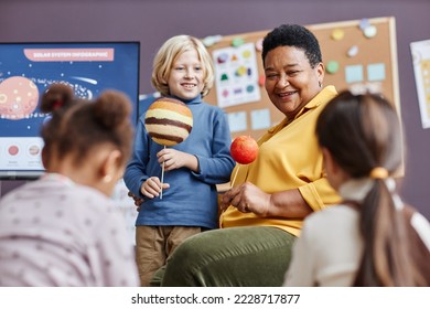 Focus on happy mature teacher and cute little boy with planet models during discussion of solar system at lesson in kindergarten - Powered by Shutterstock