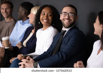 Focus On Happy Young African American Woman Sitting In Row Line With Diverse Business People, Listening To Smiling Lady. Motivated Mixed Race Job Applicants Communicating In Queue Before Interview.