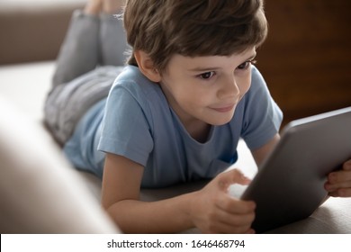 Focus On Interested Smiling Little School Boy Playing Online Game On Computer Tablet. Happy Small Kid Child Using Educational Applications On Electronic Device Or Watching Cartoons Alone At Home.