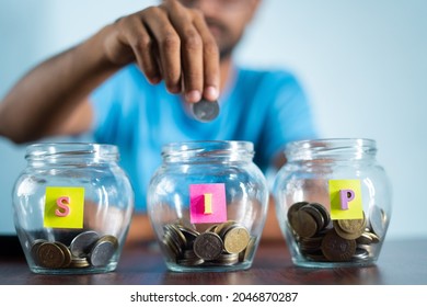 Focus on jar, Man from behind placing coins inside the jar - Concept of monthly SIP or systematic investment plan.