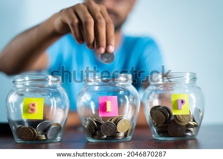 Focus on jar, Man from behind placing coins inside the jar - Concept of monthly SIP or systematic investment plan.