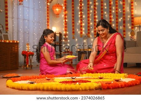 focus on kid,Happy Indian young Mother with daughter preparing Diwali rangoli for celebration - concept of home decoration, family bonding and religious custom.