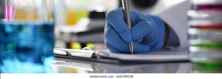 Focus on laboratory worker hand making notes in journal. Person writing down observations and results in report. Lab office investigation and analysis concept