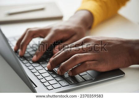 Focus on left hand of young African American employee or student typing on laptop keyboard while working over business or school project