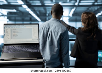 Focus on lines of code on laptop screen used by data center engineers in blurry background to execute security patches. Close up of script on notebook ran by server hub employees scanning equipment