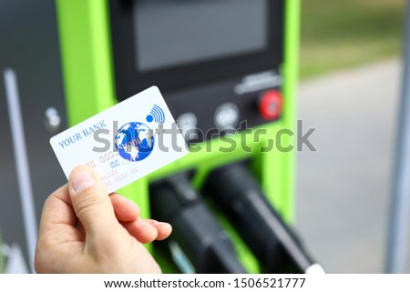 Focus on male hand with bankcard. Different ways of payments on electric car charging station. Electronic money and newest transport technology concept. Blurred background