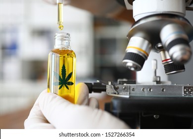 Focus on male hand holding glass bottle with cannabinoid oil. Pharmacist dripping medicine drops in flask. Healthcare and marijuana concept. Blurred background