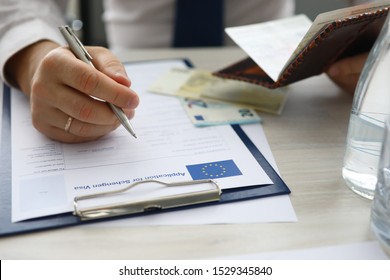Focus on male hand holding passport and writing personal data in application for schengen visa. Man sitting at office. Travelling abroad or immigration concept. Blurred background - Shutterstock ID 1529345840