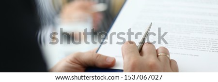 Focus on male hand holding pen and paper folder with contract. Partner checking conditions of important biz bargain in meeting room. Blurred background