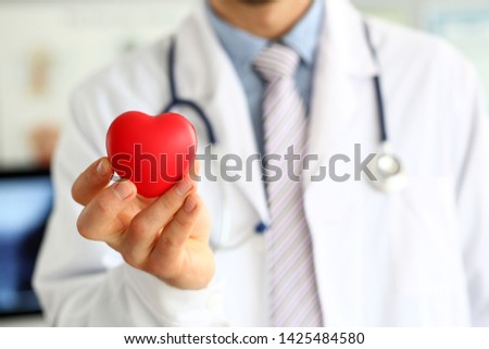 Focus on male hand with red heart-shaped symbol. Doctor wearing white uniform with stethoscope. Physician for prevent cardiovascular diseases. Medical treatment and healthcare concept