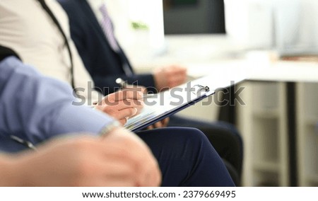 Focus on male hands holding paper folder with important agreements and writing something. Colleagues at biz seminar. Company meeting concept. Blurred background