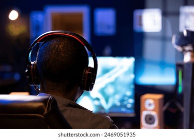 Focus on man playing videogames on computer monitor in blurry background, talking into headset. African american gamer using headphones to chat with his Esports team, close up - Powered by Shutterstock