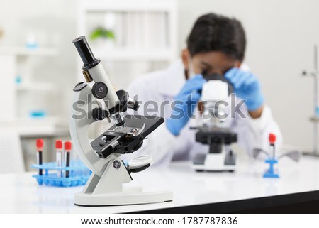 Focus on Micro Scope in front of Asian Male Scientist wear Face Mask working in Lab while Checking Blood Sample by micro scope On Background.
