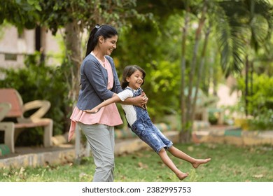 focus on mother, Cheerful indian mother playing by rotating his daughter at park - concept of weekend holidays, Carefree moments and Playful affection. - Powered by Shutterstock