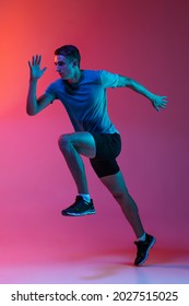 Focus On Movement. Portrat Of Professional Male Athlete, Runner Training Isolated On Pink Studio Background With Blue Neon Filter, Light. Concept Of Action, Motion, Speed, Healthy Lifestyle. Copyspace