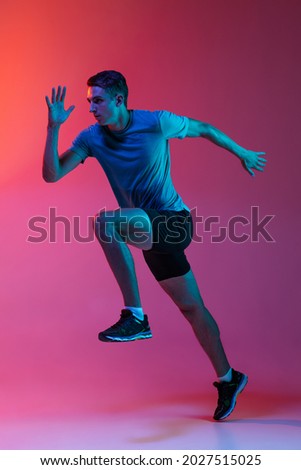 Focus on movement. Portrat of professional male athlete, runner training isolated on pink studio background with blue neon filter, light. Concept of action, motion, speed, healthy lifestyle. Copyspace