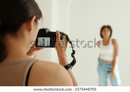 Focus on photocamera in hands of young professional photographer taking shot of female fashion model on photocamera screen