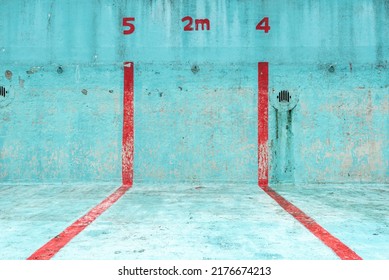 Focus on a piece of an abandoned public swimming pool in a bright blue colour with red stripes. The lanes and depth are indicated. - Shutterstock ID 2176674213
