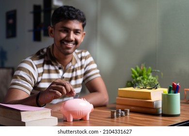 Focus On Piggy Money Bank Young Indian Student Saving Money For Future Abroad Education By Placing Money On Piggy Bank While Reading At Home - Concept Of Finance, Future Planning Or Aspirations