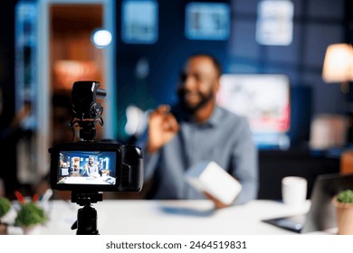 Focus on professional video production camera used for capturing footage of content creator in blurry background doing products unboxing for online audience, showcasing different tech electronics - Powered by Shutterstock