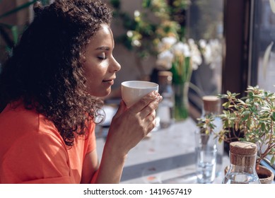 Focus On Profile Of Serene Woman Sitting In Cafe. She Is Holding Cup Of Coffee And Smelling Its Delicious Flavor. Copy Space In Right Side