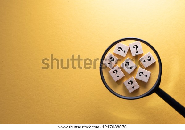 Focus on Question Mark symbol on a wooden tiles using
magnifying glass against yellow background. Concept of Q and A,
questions and faq