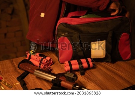 Focus on red dynamite, unrecognizable militent or soldier preparing by placing time bomb with dynamite and gun inside the bag.