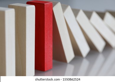 Focus on red object refusing to bend under harsh circumstances affecting other in irreversible sequence of domino effect. One special tile out of many is stopping falling. Strong individual concept - Shutterstock ID 1550862524