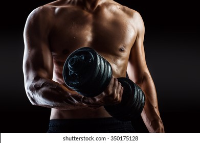 Focus On Right Torso. Dark Contrast Shot Of Young Muscular Fitness Man Torso And Arm. Bodybuilder With Beads Of Sweat Training In Gym. Working Out With Dumbbells On Black Background