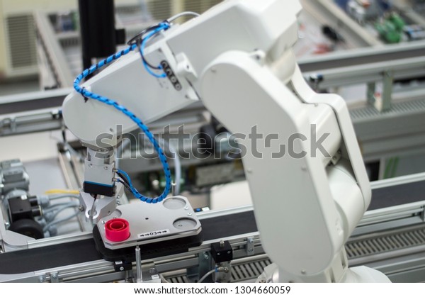 Focus on robotic arm\'s gripper. Industry 4.0\
concept; artificial intelligence in smart factory. Robot picks up\
the product from automated car on the manufacturing line. Selective\
focus.