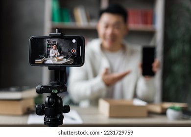 Focus on screen of smartphone, pleasant asian man filming video on modern phone camera while opening parcel box with new smartphone. Concept of people, technology and blogging. - Shutterstock ID 2231729759