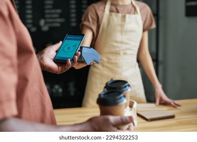 Focus on smartphone held by mature African American male consumer during contactless payment for coffee by counter desk in cafe - Powered by Shutterstock