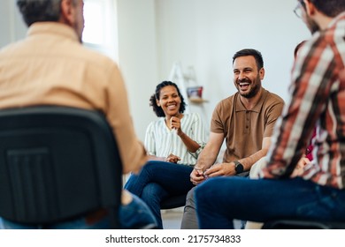 Focus on the smiling man, talking with people of all ages, during the group therapy.