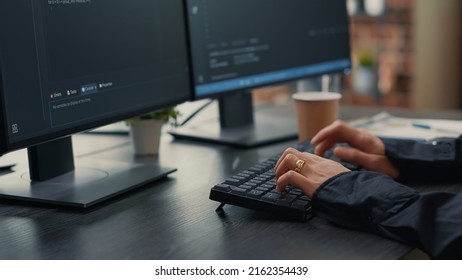 Focus on software developer hands typing source code on keyboard while looking at computer screens with programming interface. Programer sitting at desk with clipboard writing algorithm.