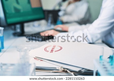 Focus on stack of white folders with top secret sign on cover containing information about clinical experiment that cannot be divulged