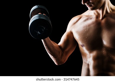 Focus On Stomach. Dark Contrast Shot Of Young Muscular Fitness Man Stomach And Arm. Bodybuilder With Beads Of Sweat Training In Gym. Working Out With Dumbbells On Black Background