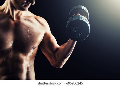 Focus On Stomach. Dark Contrast Shot Of Young Muscular Fitness Man Stomach And Arm. Bodybuilder With Beads Of Sweat Training In Gym. Working Out With Dumbbells On Black Background