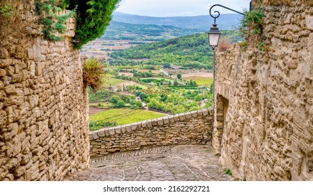 Focus on stone walls and a cobblestone street of the medieval village of Gordes in the Luberon Region of Provence, France, overlooking a wide valley of cultivated fields, orchards and vineyards below. - Shutterstock ID 2162292721