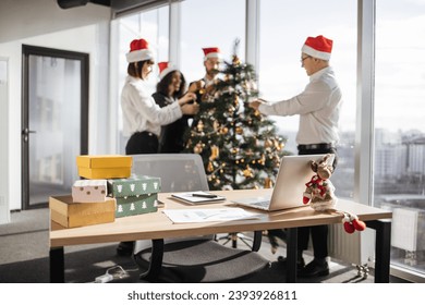 Focus on table with gifts on blur background of multiethnic group of coworkers decorating christmas tree, putting festive ornaments in startup office. - Powered by Shutterstock