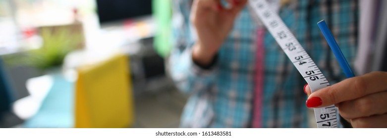 Focus On Tender Female Hands Holding Important Measuring Utility And Wearing Fashionable Clothes. Witty Girl Working On Significant Project. Fashioner Workshop Concept . Blurred Background