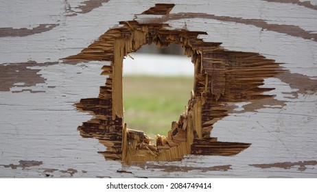 Focus on through hole in old white plywood wall. Outdoor. Closeup on splintered wood. View through hole. Surface, texture. - 15 April 2021, Montreal, Canada