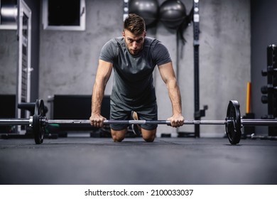 Focus on training and concentration on exercise. A young attractive man in a gray T-shirt rests his hands on a barbell and squats in the gym. Initial body posture and sports discipline - Shutterstock ID 2100033037