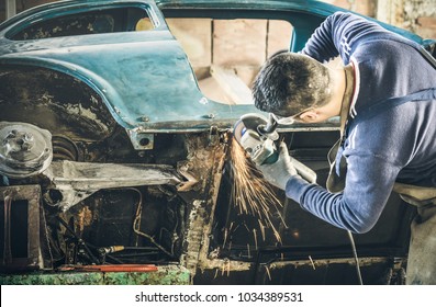 Focus On Vintage Car Body - Man Mechanical Worker Repairing With Electric Grider In Messy Garage - Work Safety With Protection Wear - Niche Expertise Concept With Guy Working With Technical Equipment