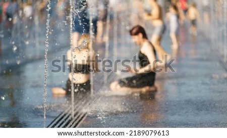 Focus on the water jets in the foreground. Defocused photography. Youth lay down among fountains in the hot summer day. Time to cool. Fresh water splashes. Concept of leisure, freshness, happiness.