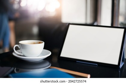 Focus On White Coffe Cup With Blank Screen Of Digital Tablet On Desk In Cafe